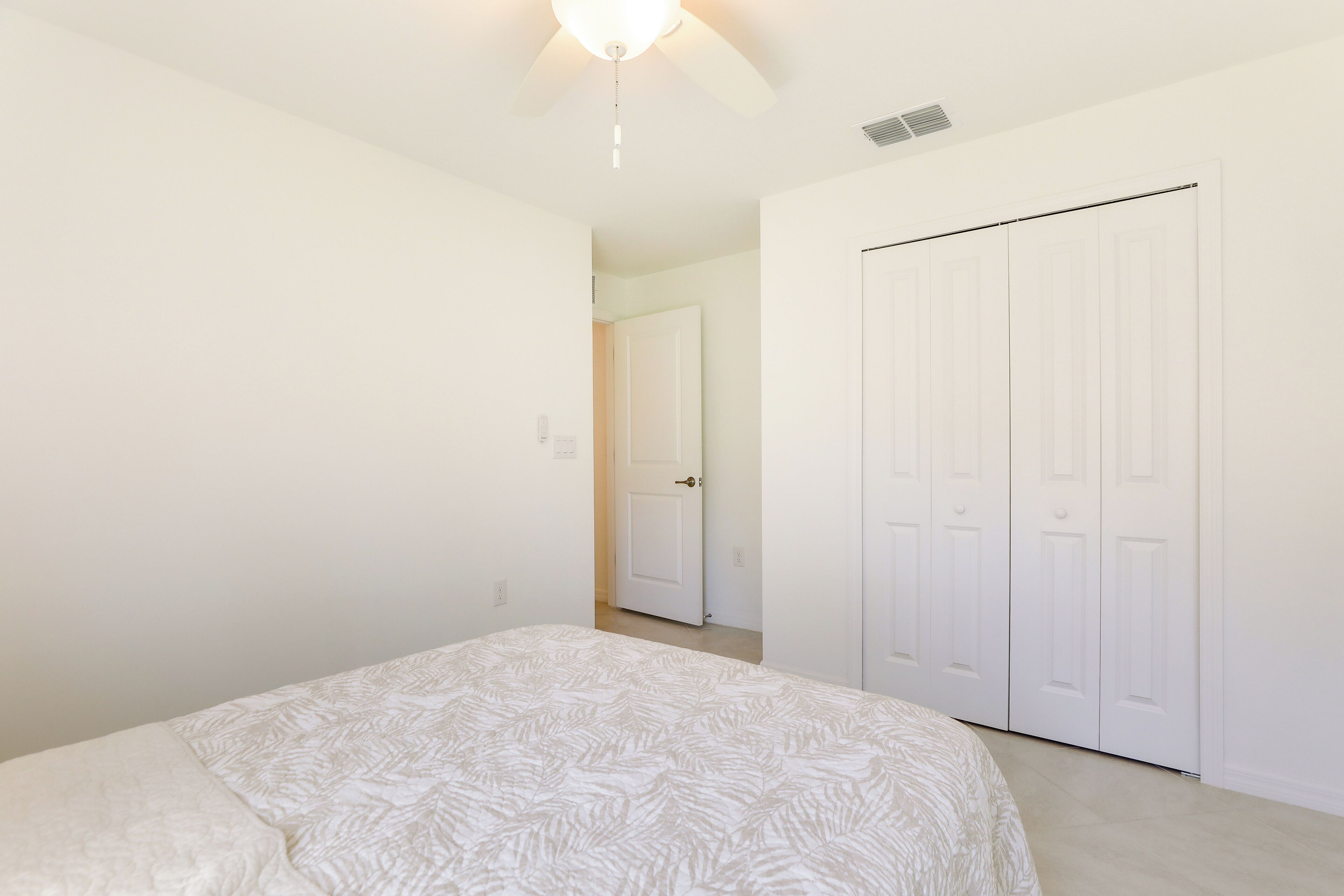 Une chambre à coucher avec un lit, un ventilateur de plafond et une porte blanche.