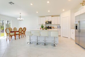 A modern kitchen with white cabinets, stainless steel appliances, and a dining area with wooden chairs and bar stools.