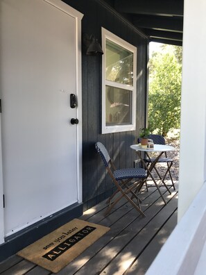 Un portico con una porta bianca, una finestra, un tavolino con sedie e un tappetino d'ingresso con la scritta 'see you later ALLIGATOR'.