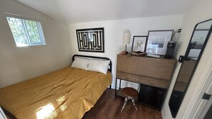 Una habitación compacta con cama, escritorio, silla, espejo y ventana.
