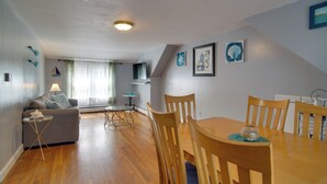 Un comedor con sillas de madera y una mesa, un sofá con una lámpara y una ventana con cortinas.