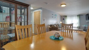 Un comedor con una mesa de madera, sillas, un aparador de vidrio y un televisor al fondo.