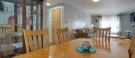 A dining area with a wooden table, chairs, a glass cabinet, and a television in the background.