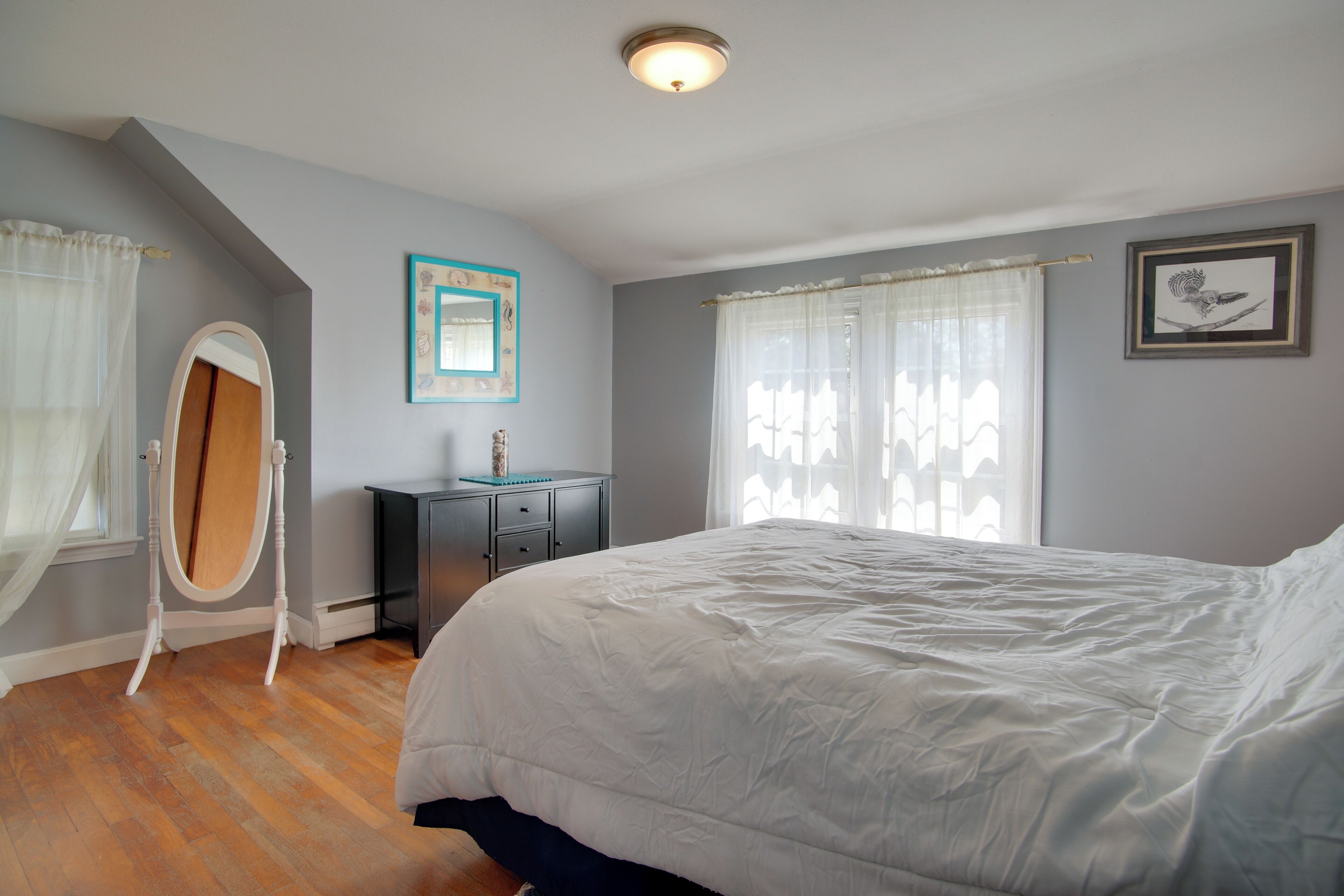 A bedroom with a large bed, a dresser, a vanity with a mirror, and a ceiling light.