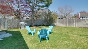 Un jardin avec une clôture en bois, un barbecue et trois chaises Adirondack bleues.