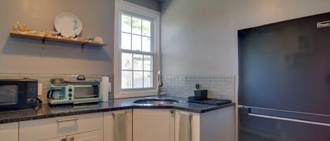 A kitchen with white cabinets, a stainless steel refrigerator, a microwave, a toaster, and a window.