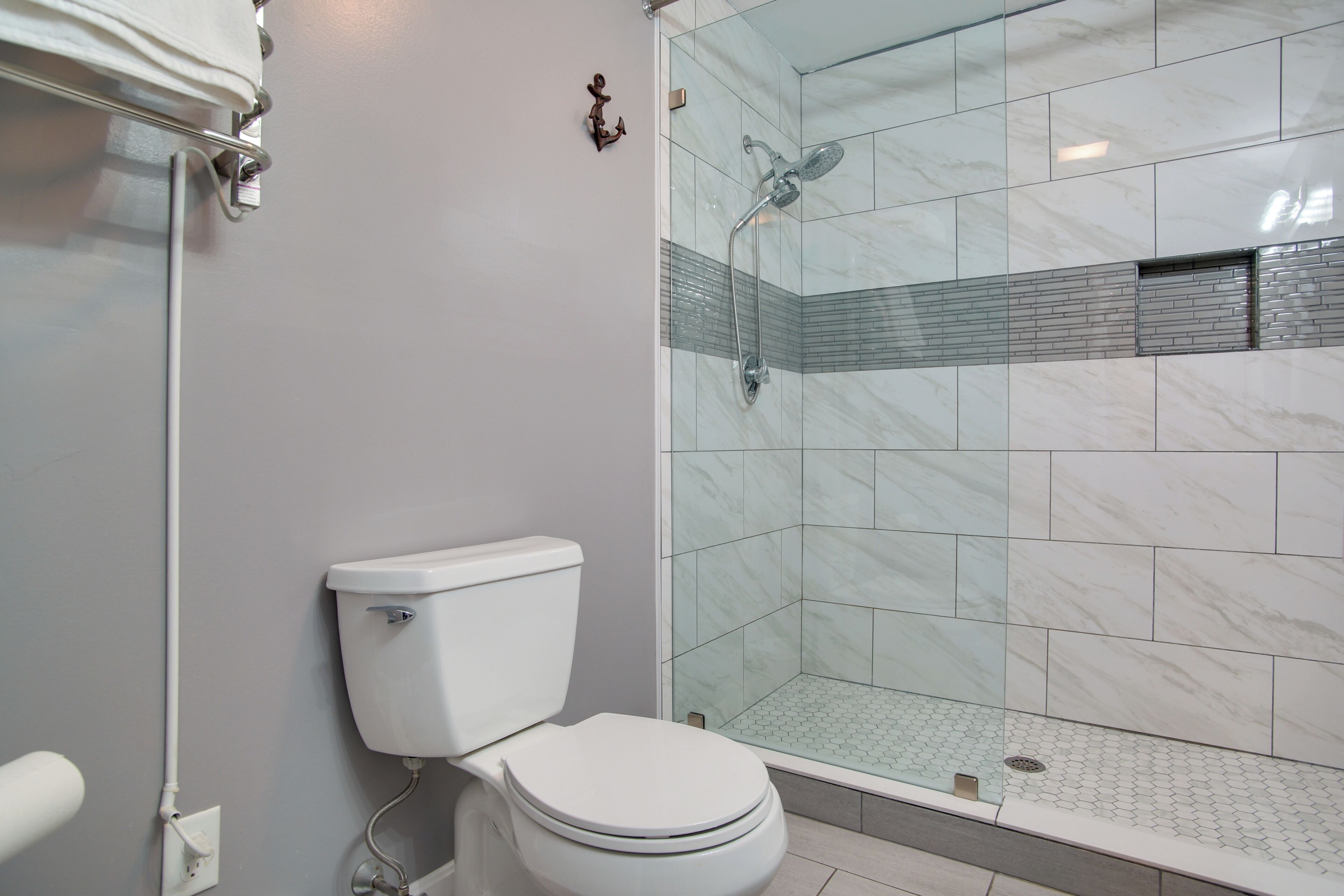 Une salle de bain avec des toilettes, une douche dotée d’une porte en verre et un mur recouvert de carreaux.