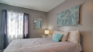 Une chambre à coucher avec un lit, des rideaux, une table de chevet, une lampe et des œuvres d’art murales.