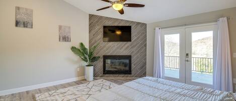 Une chambre avec un lit, un ventilateur de plafond, une cheminée, une télévision et un balcon avec des rideaux.