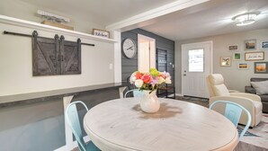 A dining area with a round table, chairs, and a vase of flowers. There are wall-mounted decorations and a clock.