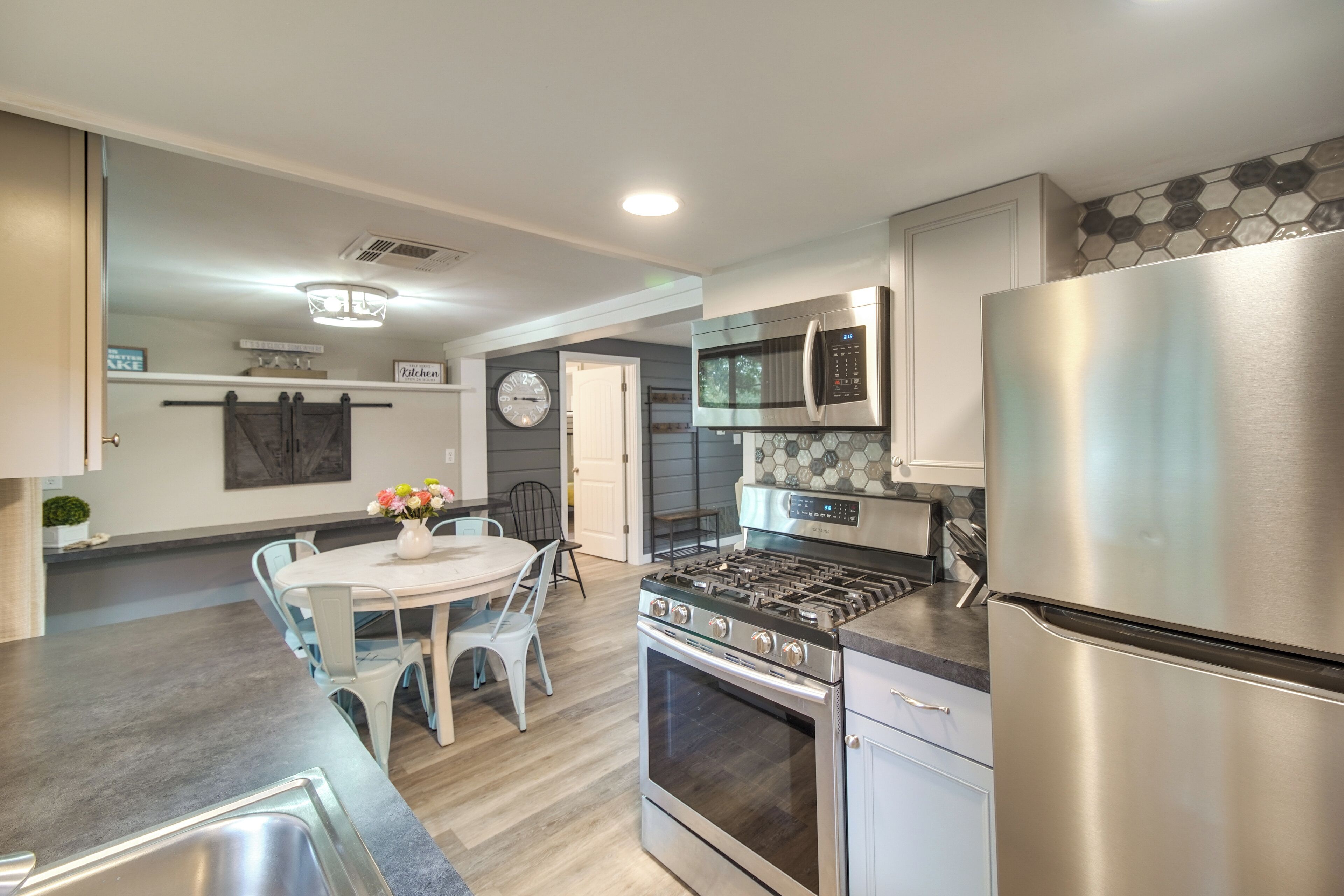 A modern kitchen with stainless steel appliances, a dining area with a white table and chairs, and a clock on the wall.