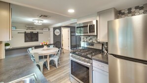 A modern kitchen with stainless steel appliances, a dining area with a white table and chairs, and a clock on the wall.
