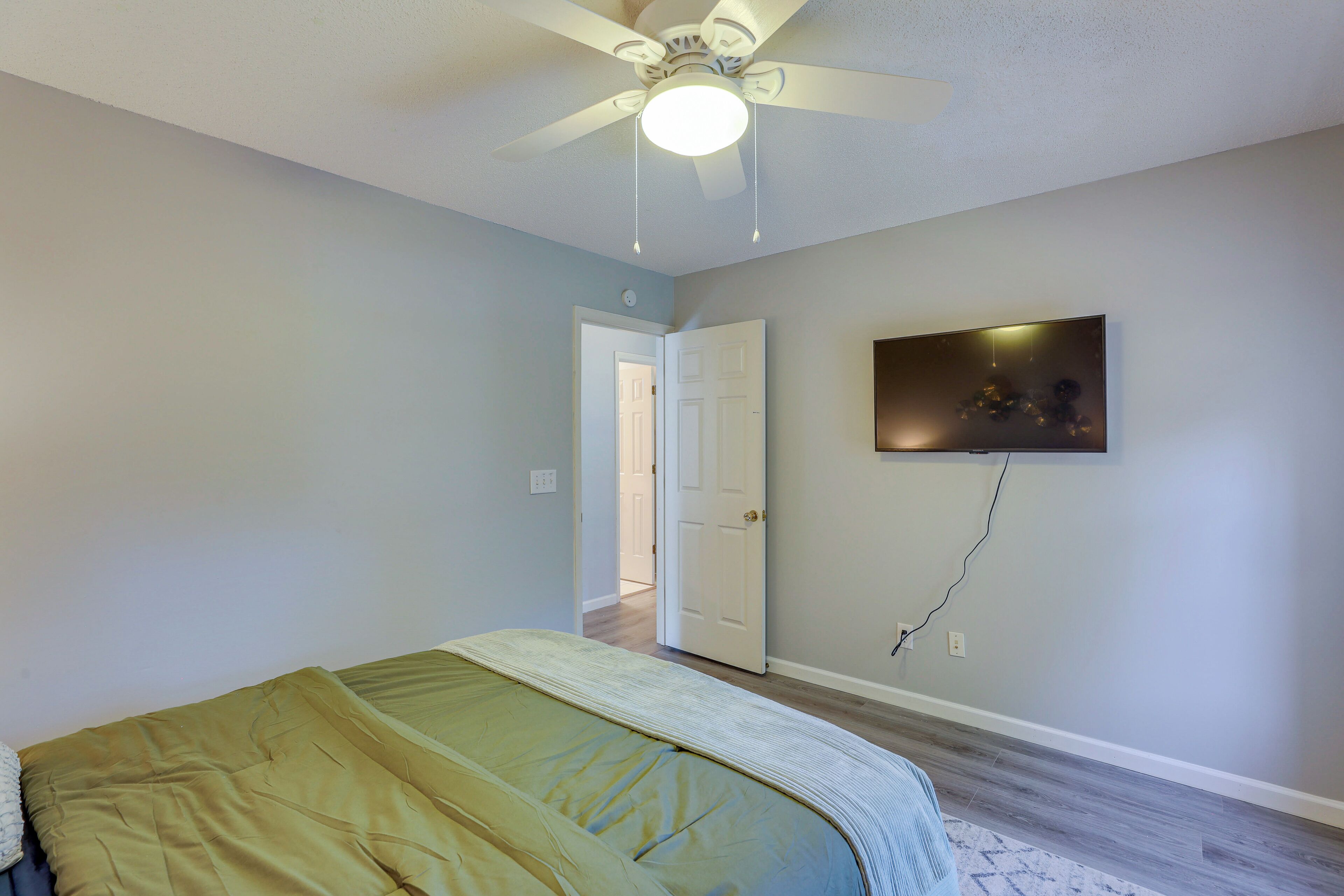 Ein Schlafzimmer mit Bett, Deckenventilator, Tür und Wand-Fernseher.