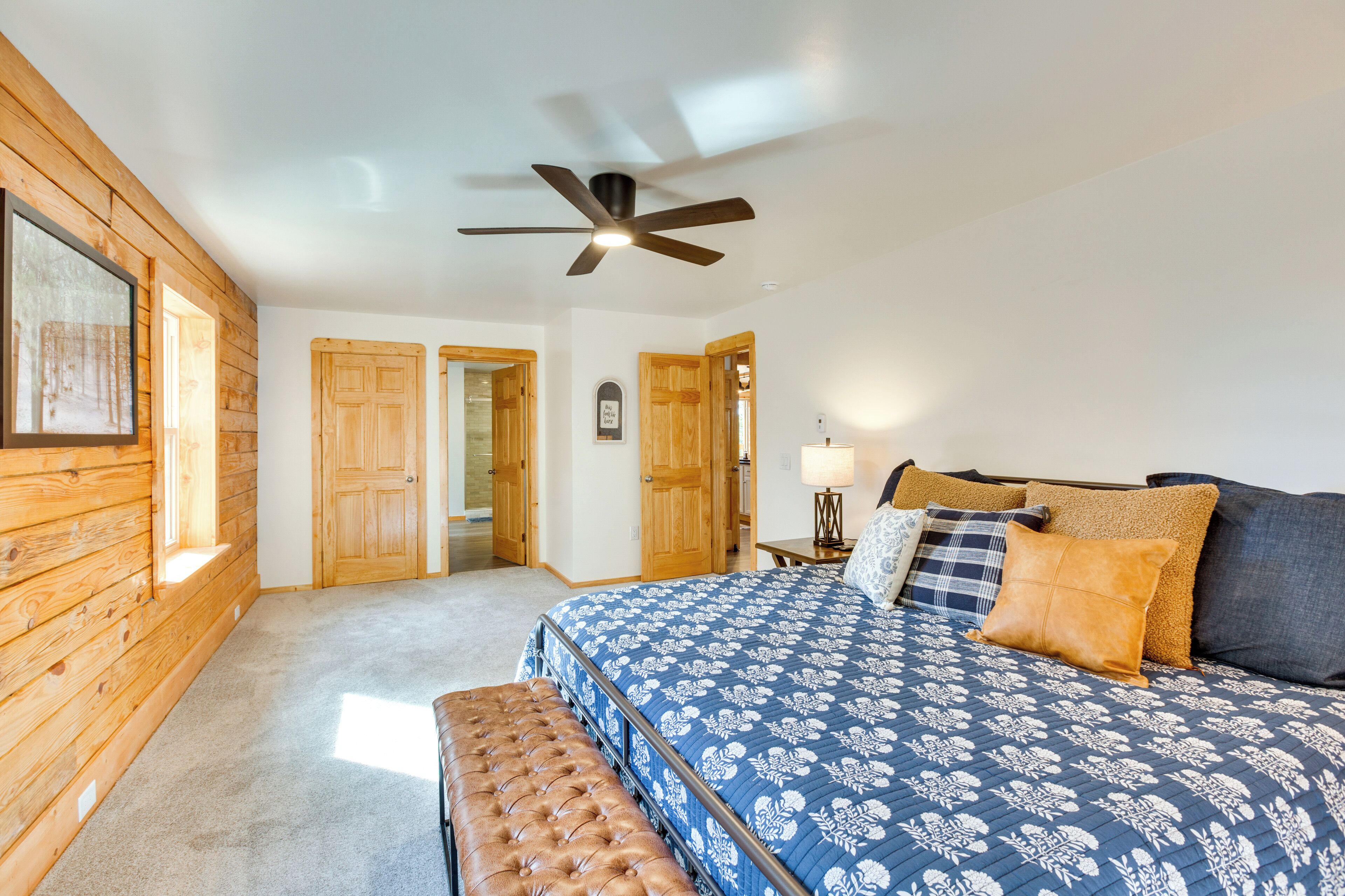 A bedroom with a large bed, wooden walls, and a ceiling fan.