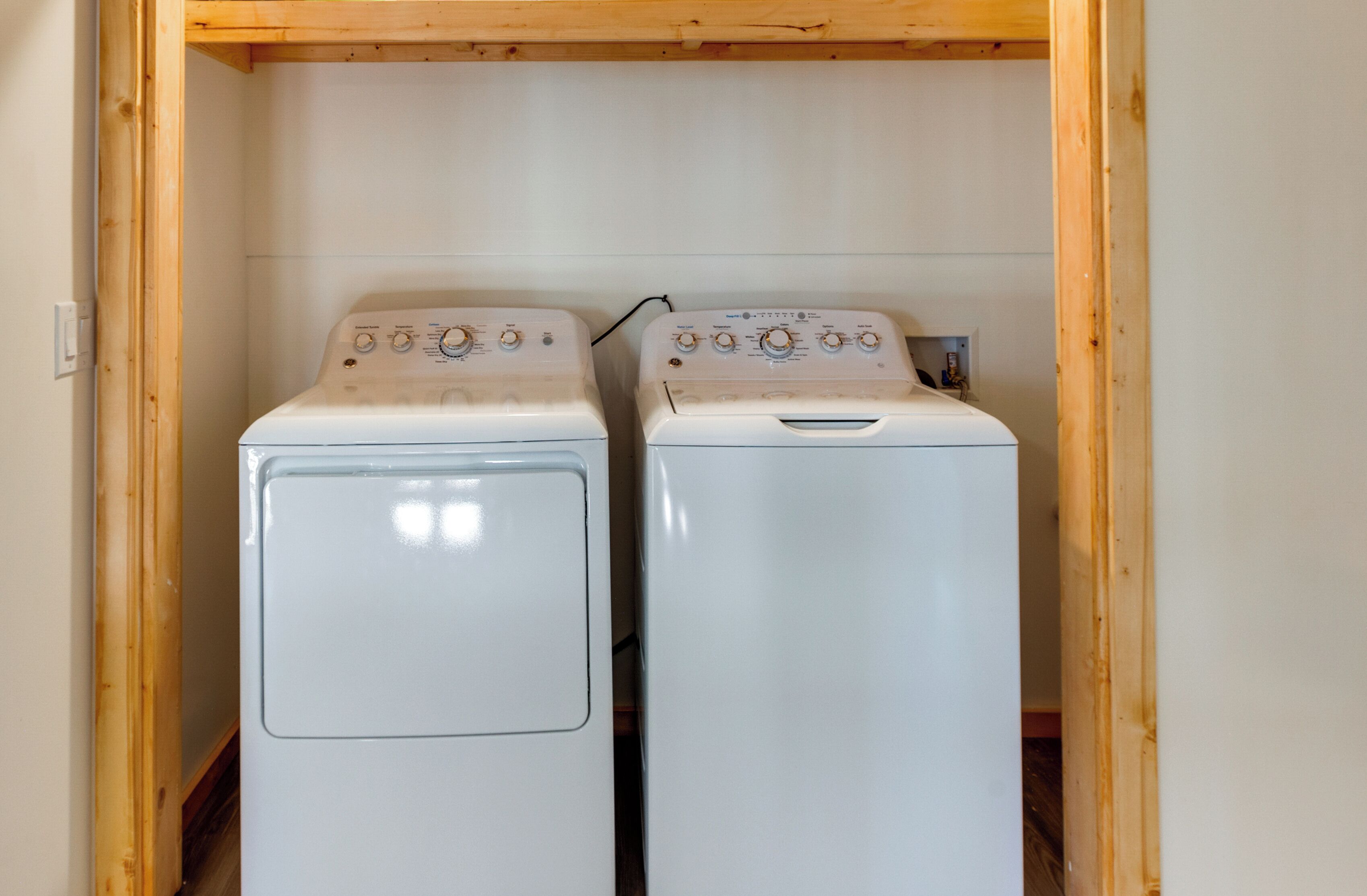 Two white front-loading washing machines in a wooden cabinet under a wooden beam.