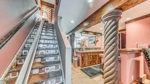 Una escalera con baldosas estampadas, un pilar de madera, y una cocina con armarios de madera y una barra.