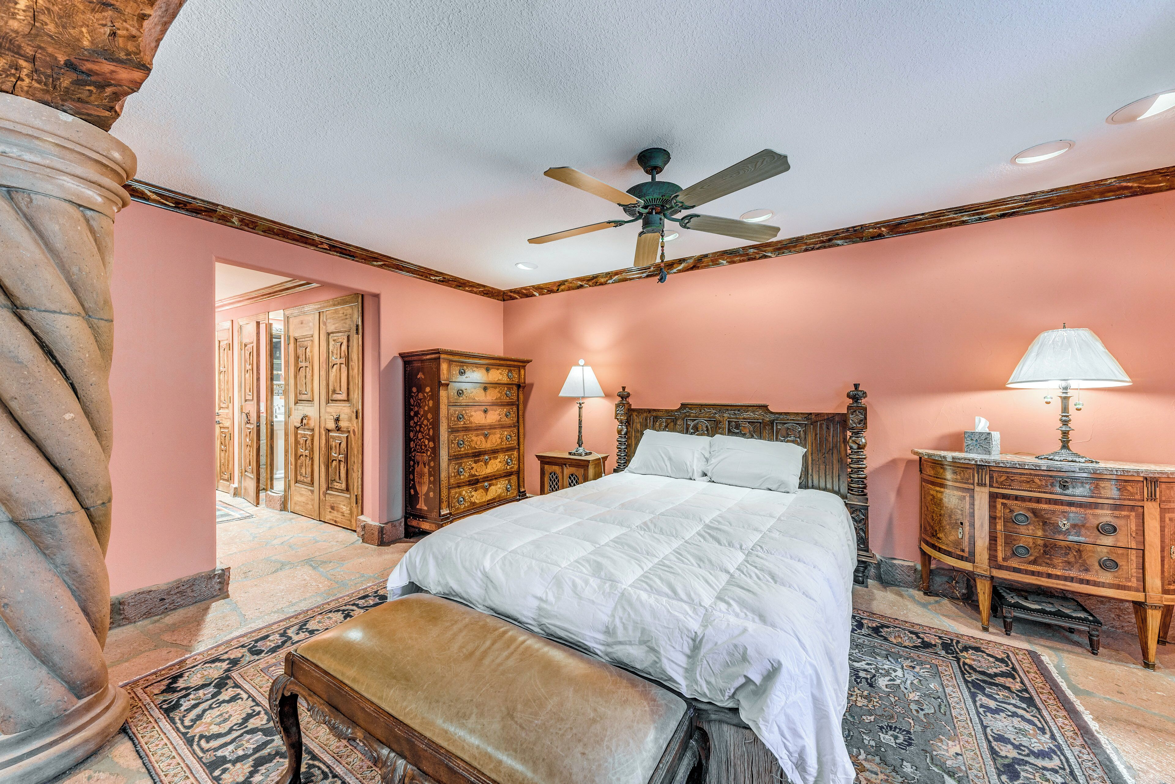 A bedroom with a large bed, wooden furniture, a ceiling fan, and a patterned rug.