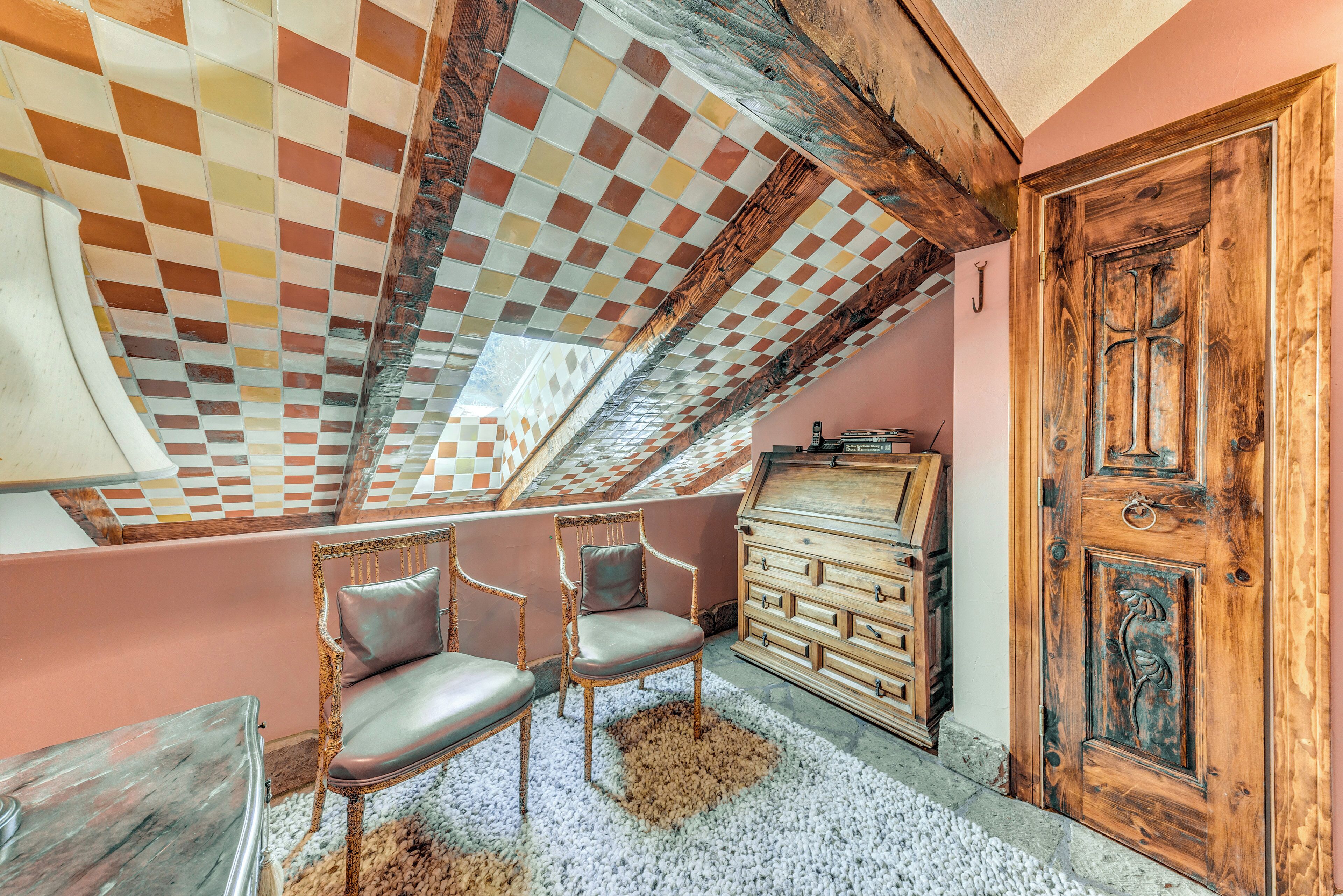 Una habitación con techo a cuadros, puerta de madera y un pequeño rincón de descanso con sillas.