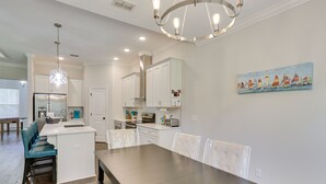 A modern kitchen with white cabinetry, a central island, and a dining area with a long table and chairs. - Family-friendly Crawfordville Home ~ 15 Mi to Fsu! (Crawfordville)