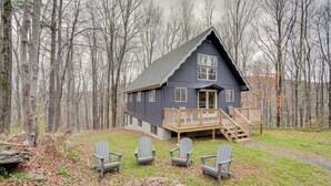 Una cabaña con terraza de madera y cuatro sillas Adirondack al frente.