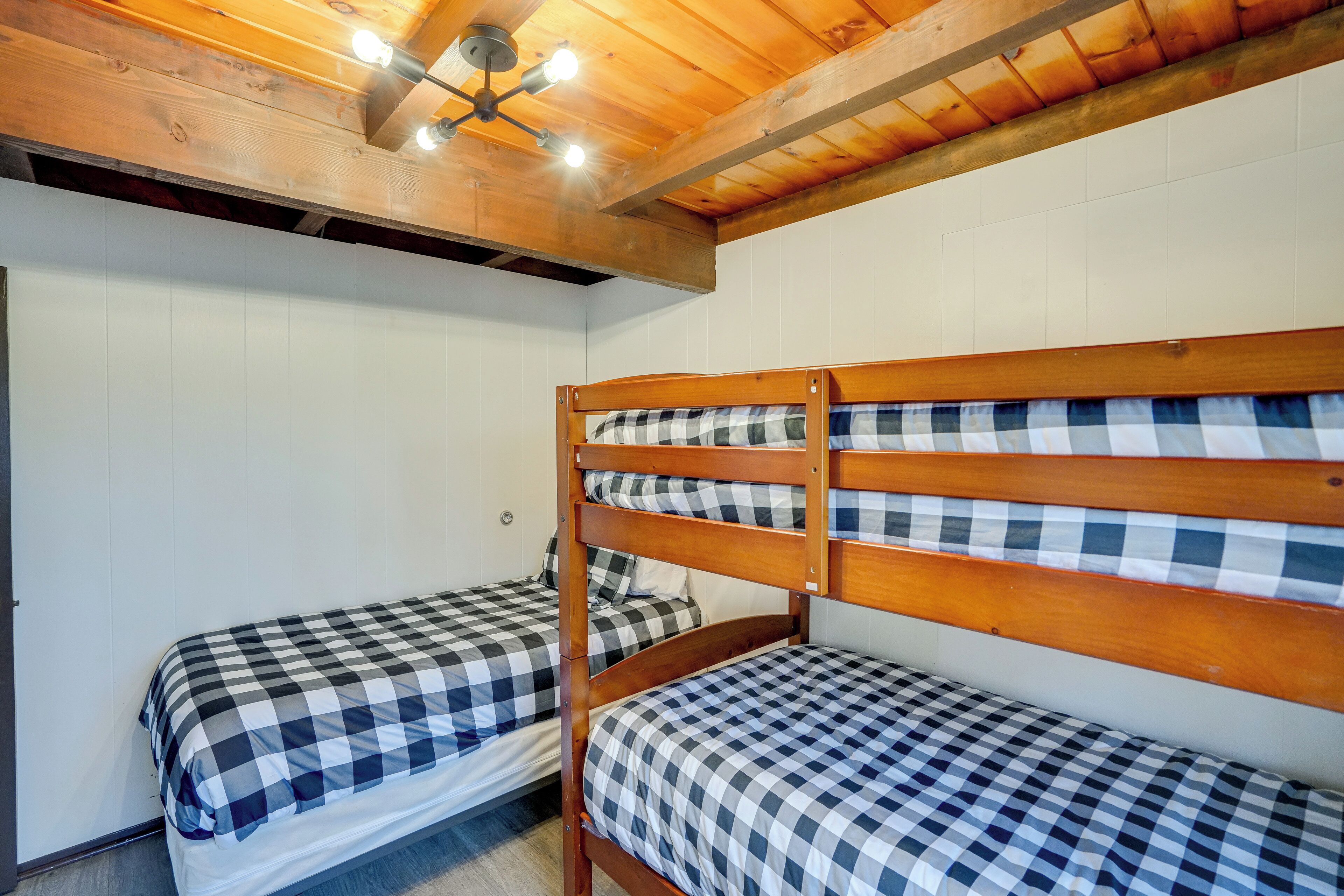 A room with two bunk beds, wooden ceiling beams, and a ceiling light fixture.