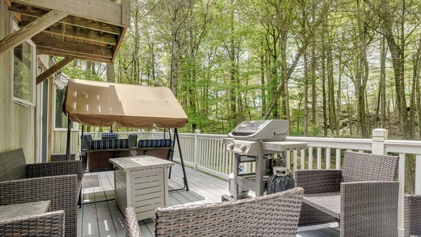 Eine überdachte Terrasse mit Rattanmöbeln, einem Grill und Blick auf einen Wald.