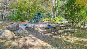 Ein Spielplatz mit Rutsche und Klettergerüsten, umgeben von Bäumen und Picknicktischen.