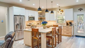 A modern kitchen with white cabinets, stainless steel appliances, a wooden dining table, and pendant lighting.