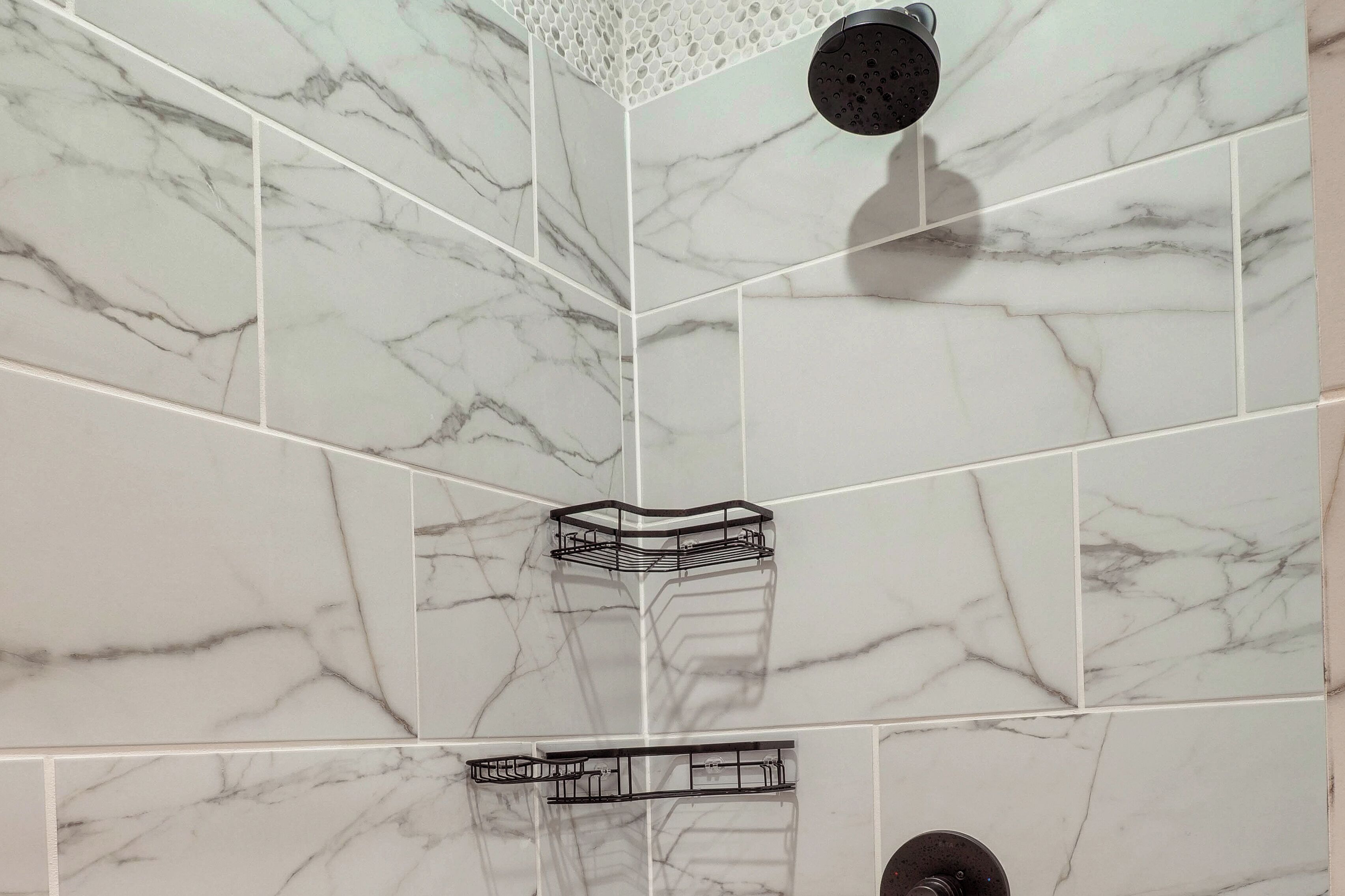 A bathroom with white marble tiles, a shower head, and a corner shelf.