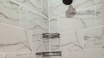 A bathroom with white marble tiles, a shower head, and a corner shelf.