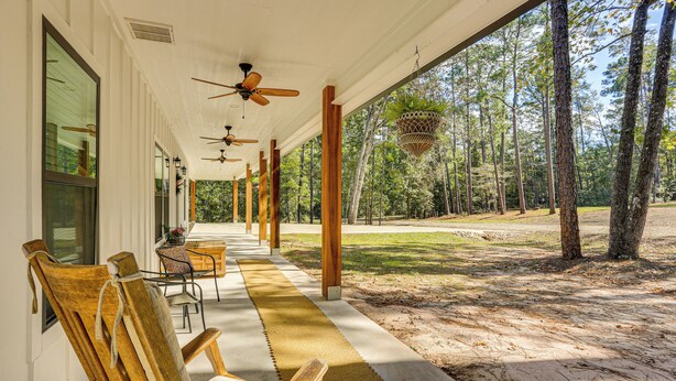 A covered outdoor seating area with wooden chairs and tables, ceiling fans, and a view of a forested area.