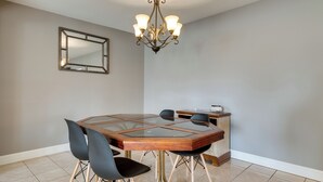 Ein Essbereich mit Glastisch, schwarzen Stühlen, einer Holzkommode, einer Chandelierleuchtre und einem Spiegel an der Wand.