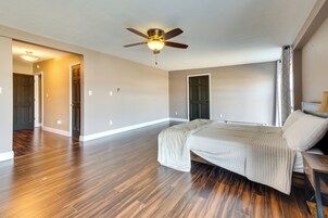 Un dormitorio amplio con suelo de madera, una cama con cabecera, un ventilador de techo y una puerta que da a otra habitación.