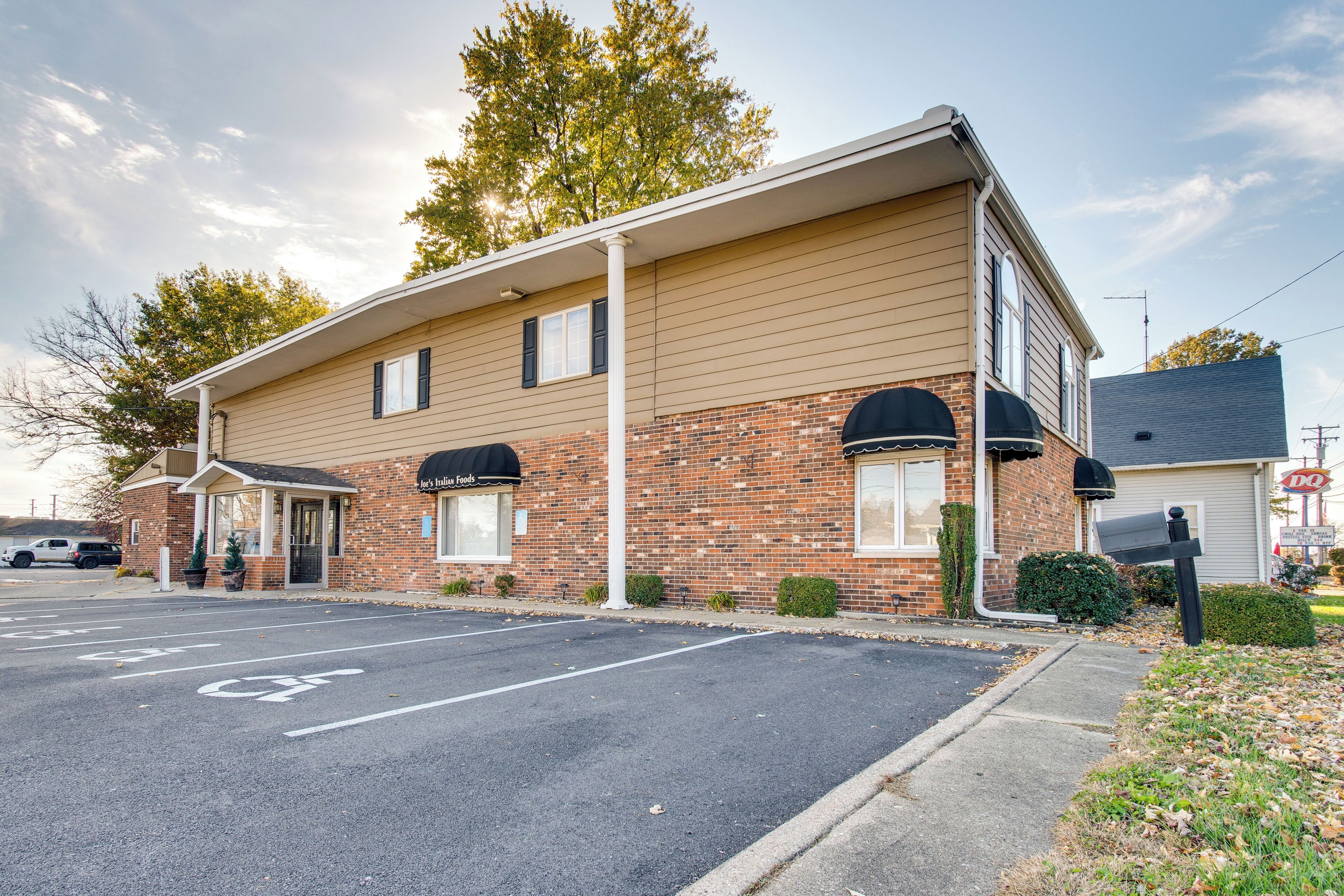 A two-story motel with a brick facade, a covered parking area, and a visible sign for a nearby restaurant.