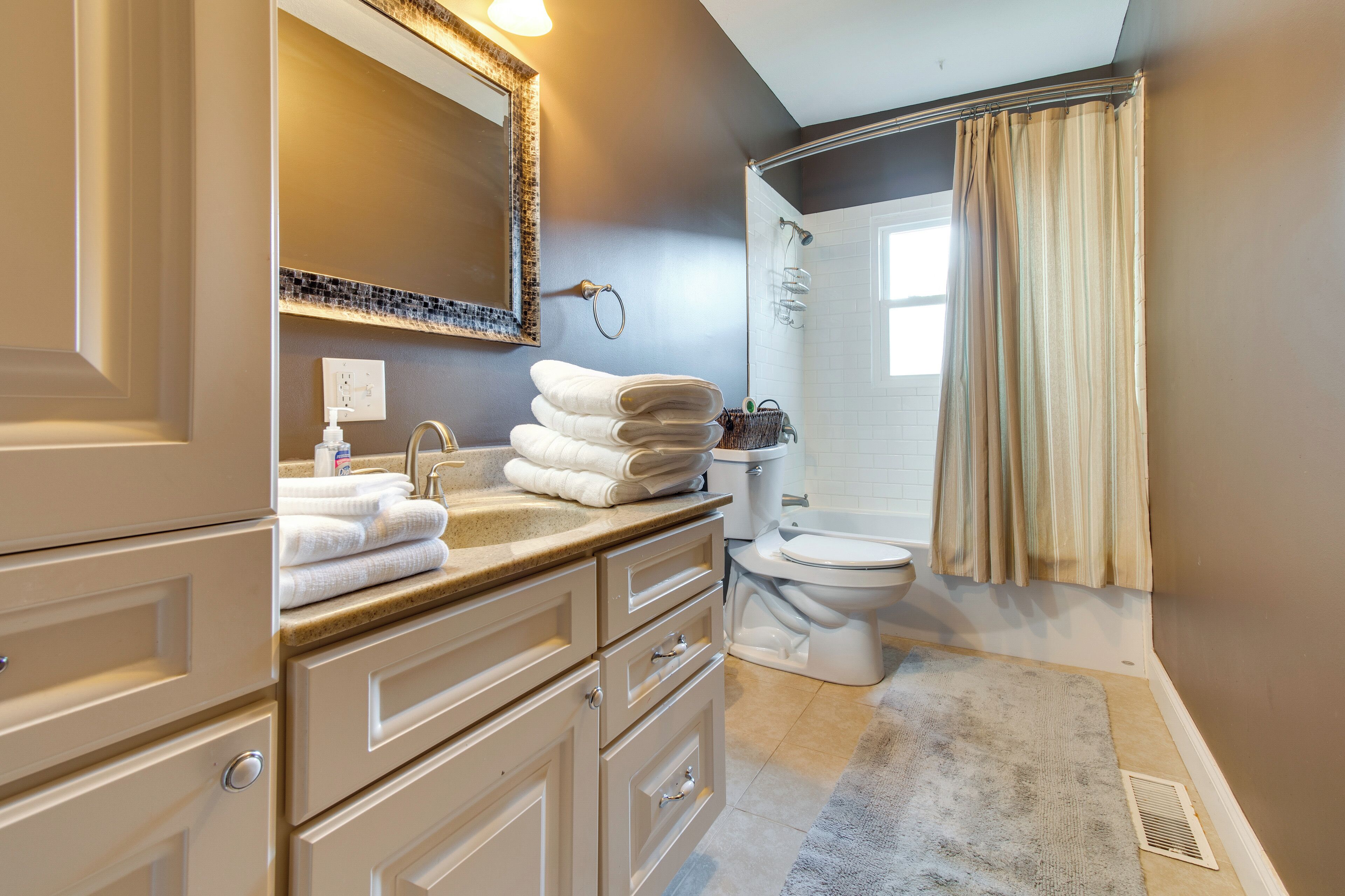 A bathroom with a sink, mirror, towel stack, toilet, and shower area.
