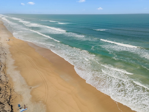 A beach with a wide sandy shore, waves, and a clear sky.