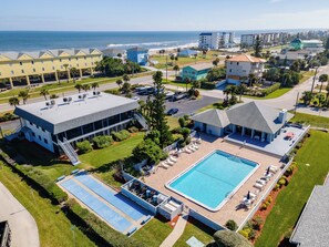 A resort with a swimming pool, tennis courts, and a view of the ocean.