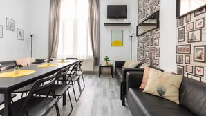 A modern living room with a dining area, featuring a black leather sofa, a dining table with chairs, and a flat-screen TV mounted on the wall. - FAMILY APARTMENT A/C FREE-BREAKFAST @OLD-TOWN (Budapest)