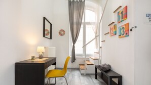 A compact room with a desk, a yellow chair, a bench with towels, a window with curtains, and wall clocks. - FAMILY APARTMENT A/C FREE-BREAKFAST @OLD-TOWN (Budapest)