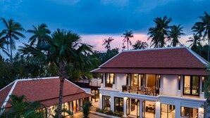 A two-story house with a swimming pool, surrounded by palm trees and a sunset sky.