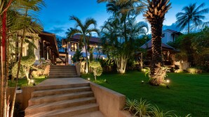 A well-lit outdoor staircase leading to a building, surrounded by lush greenery and palm trees.