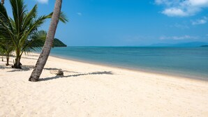 A beach with clear blue water, a sandy shore, and palm trees.
