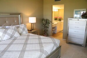 A bedroom with a bed, bedside lamp, potted plant, and a dresser.