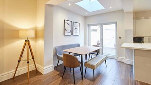 Un espace repas moderne avec un plancher en bois, une table à manger, un banc et un lampadaire sur trépied.
