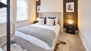 Une chambre à coucher avec un lit, des tables de chevet, un radiateur et des œuvres d’art accrochées aux murs.