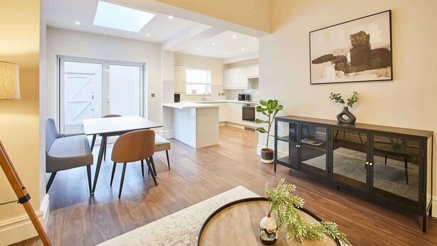 Une cuisine moderne dotée d’un îlot central, d ’un coin repas avec une table et des chaises, et d’une console sur laquelle sont posés un vase et une plante.
