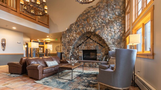 A lobby with a stone fireplace, leather sofas, a coffee table, and a large window. - Expedition Station Powder Days Condo: Ski In, Ski Out Keystone Retreat (Keystone)