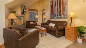 A spacious living room with leather sofas, a wooden coffee table, and a stone fireplace. - Expedition Station Powder Days Condo: Ski In, Ski Out Keystone Retreat (Keystone)