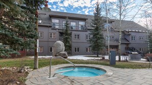 A pool area with a stone deck, a rock feature, and a building with multiple windows and balconies in the background. - Expedition Station Powder Days Condo: Ski In, Ski Out Keystone Retreat (Keystone)