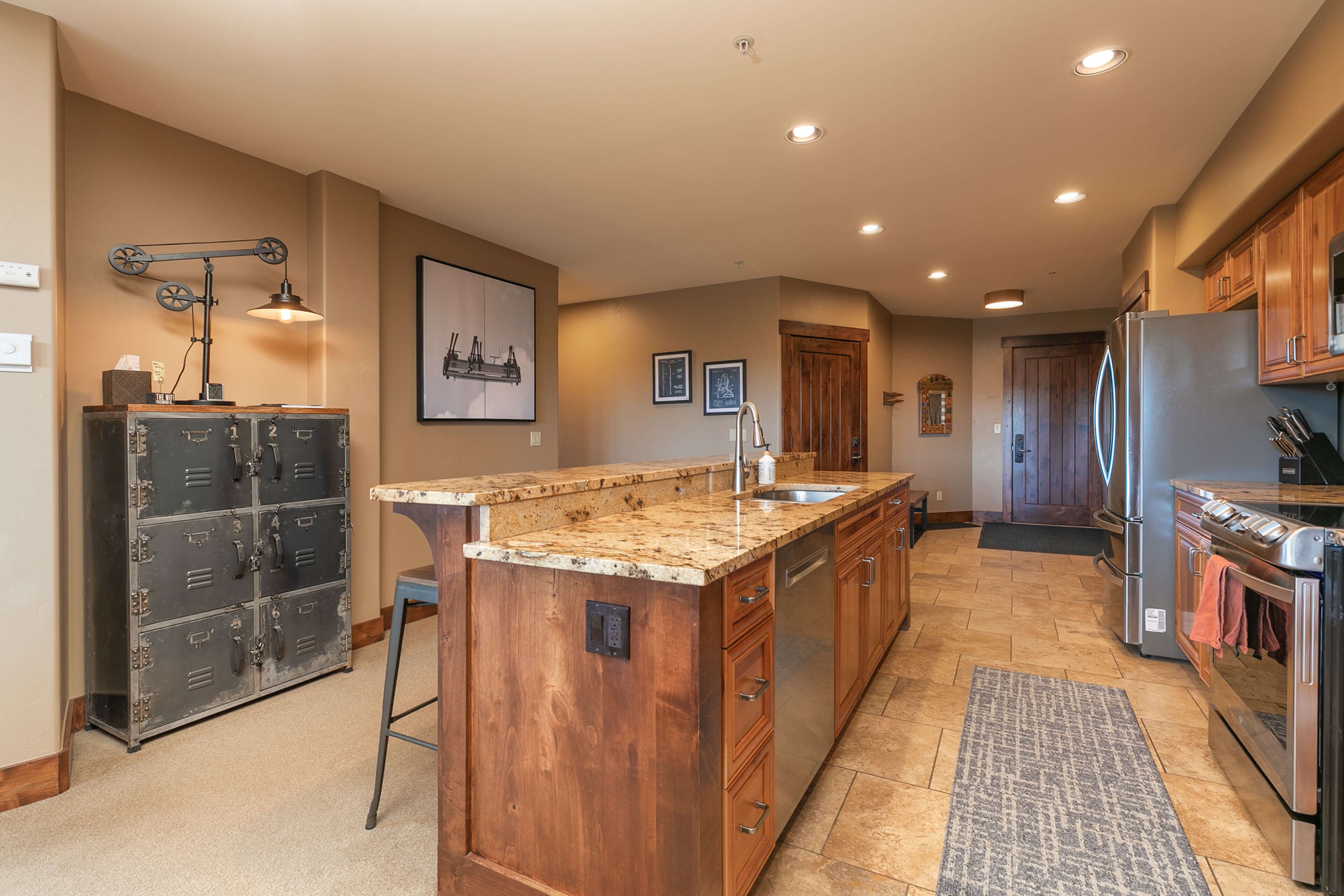 A kitchen with a central island, wooden cabinets, stainless steel appliances, and a vintage-style lamp.